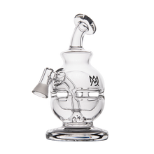 The MJ Arsenal Royale Vape Edition is a clear glass dab rig with a rounded base, angled mouthpiece, side bowl, stylized face design, and black front logo—ideal for pairing with your favorite vaporizer pen.