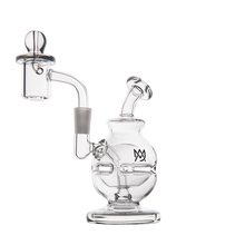 The MJ Arsenal Royale Mini Dab Rig is made of clear borosilicate glass with a round base, angled mouthpiece, and attached quartz banger. It features a decorative logo on the front and is shown on a white background.