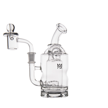 The MJ Arsenal Turbine Mini Dab Rig, made of clear borosilicate glass, features a bent mouthpiece, side chamber, removable bowl, and a small logo on the main chamber. It is displayed against a white background.
