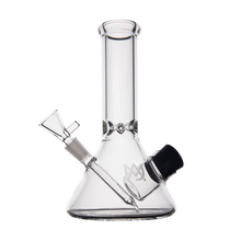 The MJ Arsenal Cache Bong is a clear borosilicate glass beaker-style bong with a cylindrical neck, angled downstem, removable bowl, black-rimmed base opening, and a subtle logo on the side.
