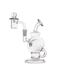 The MJ Arsenal Atlas Mini Dab Rig is a compact water pipe made from clear borosilicate glass, featuring a spherical chamber, angled mouthpiece, banger attachment, loop handle at the base, and a subtle black logo on the body. Shown on a white background.