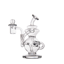 The MJ Arsenal Mini Jig Mini Dab Rig is a clear glass piece with intricate curves, a wide base, bent mouthpiece, side bowl attachment, and built-in storage jar—shown on a plain white background.