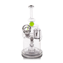 The MJ Arsenal The iLL-ien Dab Rig is a clear glass water pipe with a cylindrical base, side bowl, green accent, intricate internal chambers, and a straight neck mouthpiece.