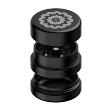 The Flower Mill 2" Next Gen Standard Grinder is a black aluminum grinder featuring a decorative floral top and multi-chamber design for grinding and storage.