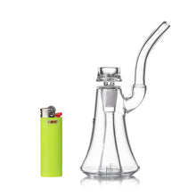 The MJ Arsenal Lumina Bubbler, made of clear borosilicate glass with a curved mouthpiece, stands beside a bright green Bic lighter on a white background.