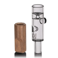 The MJ Arsenal Alpine Series Ridge Chillum Taster One Hitter, made of clear borosilicate glass in a cylindrical shape, stands upright beside a small, smooth wooden case on a white background.