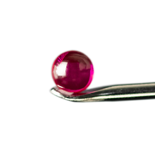A vibrant, round MJ Arsenal Ruby Terp Pearl (6mm) is delicately held at the tip of a metal tweezer against a white background, resembling an exquisite gem.