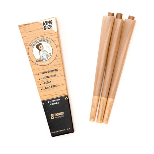 A pack labeled Blazy Susan Unbleached Paper Cones is shown beside three brown king size pre-rolled cones. The pack highlights slow burning, ultra-thin, vegan, GMO free features and contains 3 premium cones.