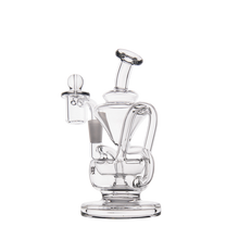 The MJ Arsenal Claude Mini Dab Rig is a clear glass recycler featuring an intricate design with curved tubes and a central chamber, displayed against a plain white background.