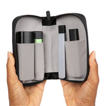Two hands hold open a small PAX Smell Proof Bag with mesh pockets, showing three cylindrical containers and a slim rectangular device inside, against a white background.