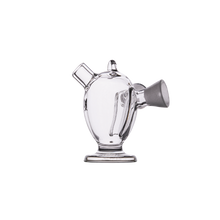 The MJ Arsenal Dubbler Original Double Bubbler is a clear borosilicate glass piece with an oval body, handle, side spout, wide base, and small top opening—ideal for precise water filtration against a plain white background.