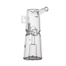 The MJ Arsenal Turret Mini Dab Rig features clear borosilicate glass, a cylindrical body, angled mouthpiece, decorative front bow, and an internal percolator—combining style and portability. Displayed on a plain white background.