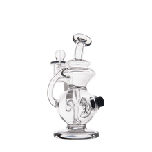 The MJ Arsenal Mini Jig Mini Dab Rig is a clear glass piece with intricate curves, a rounded base, side handle, mouthpiece, and built-in storage jar, shown against a plain white background.