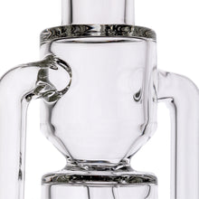 Close-up of the MJ Arsenal Alpine Series - Apex Mini Rig, a clear glass piece featuring cylindrical and tubular shapes with smooth curves. Its complex double uptake recycler design is typical of premium glass water pipes.