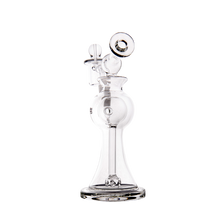 The MJ Arsenal Apollo Mini Dab Rig is a clear borosilicate glass water pipe with a wide, round base, narrow neck, and curved mouthpiece. It features intricate glasswork and attachments to preserve flavor when smoking or vaporizing.