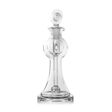 The MJ Arsenal Apollo Mini Dab Rig, made of clear borosilicate glass, features a bulbous body, narrow neck, and wide base to enhance flavor preservation. It is shown with a round stopper on a plain white background.