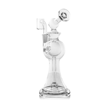 The MJ Arsenal Apollo Mini Dab Rig is a clear borosilicate glass water pipe with a round chamber, angled mouthpiece, and side attachment. Its wide base offers stability and preserves flavor, making it ideal for smoking or vaporizing substances.