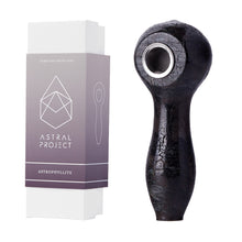 A dark, polished Gemstone Spoon Pipe stands upright beside its white and purple Astral Project box featuring "Astrophyllite," a geometric logo, and a simple pipe illustration—an elegant choice for healing gemstone fans.
