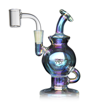 The MJ Arsenal Atlas Mini Dab Rig is a small, iridescent compact dab rig with a rounded body, angled neck, and clear quartz banger attachment for smoking concentrates, shown against a white background.