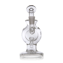 The MJ Arsenal Atlas Mini Dab Rig is a clear borosilicate glass piece with a round base, cylindrical neck, and angled mouthpiece. Its modern, sculptural design stands upright on a white background for a sleek look.