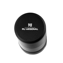 The MJ Arsenal Capsule Grinder Dugout is a black cylindrical container with a flat, white-printed lid featuring the MJ Arsenal logo, combining a portable dugout and herb grinder, shown against a white background.