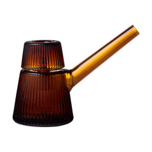The NWTN Home Deco Bubbler is a ribbed, amber-hued borosilicate glass piece with a long angled spout and coordinating cup on top, displayed against a white background.