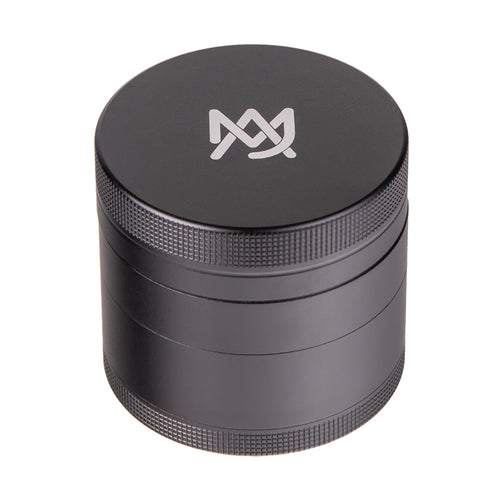 The MJ Arsenal 4 Piece Grinder is a black cylindrical aluminum grinder with textured edges and a white geometric logo on the lid, displayed on a white background.
