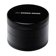 The Human Grade Grinder 4C (2.5") is a black, cylindrical aluminum herb grinder with "HUMAN GRADE" in white on the lid, featuring textured edge grips and a smooth matte finish for stylish, functional use.