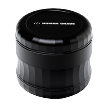 The Human Grade Grinder 6M (2.5") is a black, cylindrical aluminum herb grinder with grooved sides, a flat lid reading HUMAN GRADE in white, and a modern metallic finish for ergonomic grip.