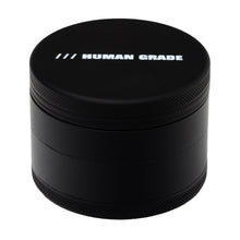 The Human Grade Grinder 4R (2.5") is a black, cylindrical 4-piece grinder with a screw-on lid, white HUMAN GRADE branding on top, textured grips on lid and base for easy use, and a built-in pollen catcher.