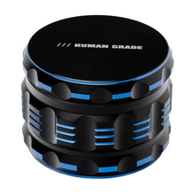 The Human Grade Grinder 5T (2.5”) is a black 4-piece aluminum grinder with blue accents, textured sides, and "HUMAN GRADE" text on the top.