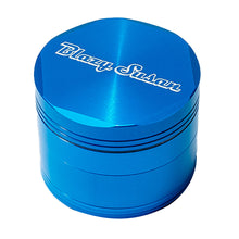 The Blazy Susan Grinder V2 is a metallic blue aluminum grinder with ridged sides and "Blazy Susan" in white cursive on top. This shiny 4-piece grinder has a large chamber for smooth herb grinding.