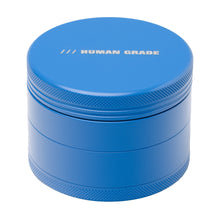 A blue, round Human Grade Grinder 4C (2.5") with textured edges, "HUMAN GRADE" in white on the lid, and comes in 4 pieces.