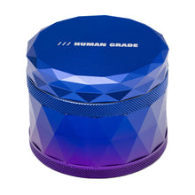 A blue, faceted, cylindrical aluminum herb grinder labeled HUMAN GRADE in white on top; this is the Human Grade Grinder 7F (2.5") with a screw-on lid, shown against a white background.