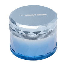 The Human Grade Grinder 7F (2.5") is a metallic, faceted 4-piece aluminum herb grinder with a textured grip, a blue gradient finish, and HUMAN GRADE printed on the flat top.