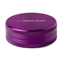 A purple, round aluminum grinder with ridged sides, 2.5" diameter, 2-piece design, and "HUMAN GRADE" printed in white on top—Human Grade Grinder 1C.