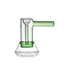 The MJ Arsenal Cove Glass Bubbler, crafted from clear borosilicate glass with a green cylindrical stem and matching handle, showcases clean lines and a modern minimalist style against a white background.