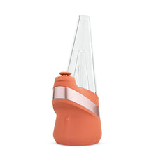 The New Peak Vaporizer stands upright on a white background, featuring a modern cone-shaped design with clear glass top, matte orange silicone base, and a metallic accent—showcasing Puffco’s iconic style.