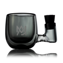 A transparent, smoky gray borosilicate glass mug with a built-in pipe on the handle and a minimalist MV logo etched on the front is displayed against a white background—the ideal match for the MJ Arsenal ISO Station.