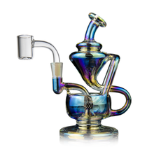 The MJ Arsenal Claude Mini Dab Rig features a colorful, iridescent glass design with a curved chamber, built-in handle, and a clear bowl attachment on the left side for a unique and intricate look.