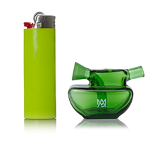 A green lighter stands upright beside the MJ Arsenal Commander Blunt Bubbler, a compact green borosilicate glass smoking pipe with an abstract design and a white logo on the front, both placed against a white background.