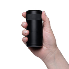 A hand holds the black MJ Arsenal Capsule Grinder Dugout with a textured grip, showcasing the sleek, portable herb grinder against a white background.