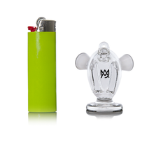 A green lighter stands upright beside the MJ Arsenal Dubbler Original Double Bubbler, a clear borosilicate glass piece shaped like a monkey with a black logo on its chest, both displayed against a white background.