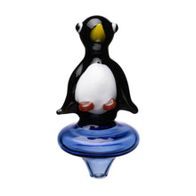 The Human Grade Penguin Carb Cap is a borosilicate glass figurine shaped like a penguin with a black body, white belly, yellow beak, and orange feet, standing on a round blue glass base.