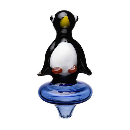 The Human Grade Penguin Carb Cap is a borosilicate glass figurine shaped like a penguin with a black body, white belly, yellow beak, and orange feet, standing on a round blue glass base.