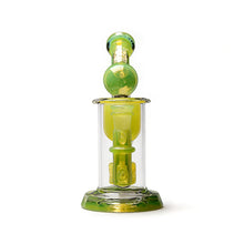 The Calibear Kickback Opal Incycler Dab Rig features green and yellow accents, a cylindrical body, seed of life percolator in its round chamber, and a sturdy base. Photographed against a white background.