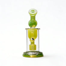 The Calibear Kickback Opal Incycler Dab Rig features green and clear glass, a cylindrical base, vertical chamber, and intricate seed of life percolator, beautifully displayed against a plain white background.