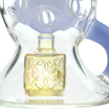 Close-up of the Calibear Infinity Loop Seed Of Life Klein Recycler, featuring clear borosilicate glass with a reflective finish, a blue handle, and a decorative yellow-tinted square element with an inner floral cutout pattern.