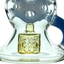Close-up view of the Calibear Infinity Loop Seed Of Life Klein Recycler, made from clear borosilicate glass with a blue handle and a geometric yellow Seed of Life percolator featuring a flower-like pattern and circular holes at the top.