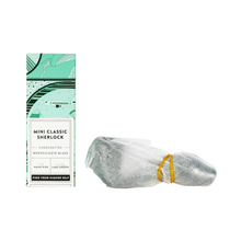 A green and white box labeled "Grav Mini Sherlock" sits beside a compact pipe with a deep bowl, wrapped in tissue paper and held together with a yellow rubber band.